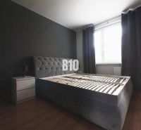 Bedroom with a dark gray bed, nightstand, and wood-patterned flooring in a 3-room apartment.