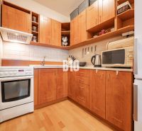 A kitchen with wooden cabinets, white appliances, and a wood-patterned floor in a two-room apartment.