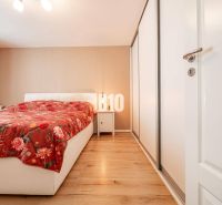 Bedroom in a 3-room apartment with a white bed, floral throw, and wood-patterned flooring.