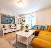 Living room of a three-room apartment with a wooden decor floor and a mustard sofa.