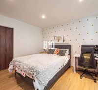 A bedroom in a family house with polka dot wallpaper, a bed, a table, and a wooden decor floor.
