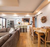 Open space in a family house with a sofa, kitchen, and dining table, wooden decor flooring.