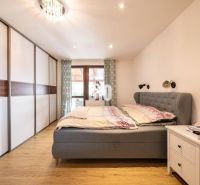 Bedroom with wood-patterned flooring, wardrobe, and upholstered bed in a family house.