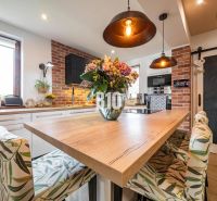 A kitchen in a family house with a dining table, a wooden decor floor, and brick cladding.