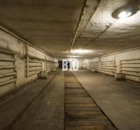 A dark underground space of a production facility with pipes on the walls and lighting.