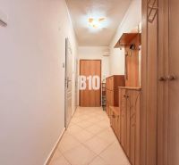 A hallway in a 3-room apartment with wooden storage furniture and tiled flooring.