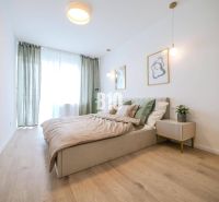 A bright bedroom in a two-room apartment with a wood-patterned floor and minimalist furniture.