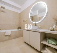 A bathroom in a 2-room apartment with a bathtub, a round mirror, and beige tiles.