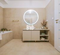 A bathroom with a round mirror and beige tiles in a 2-room apartment.