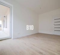 A room with a wooden floor design and large balcony doors in a 3-room apartment.