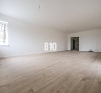 A spacious room in a 3-room apartment with a wooden decor floor and white walls.