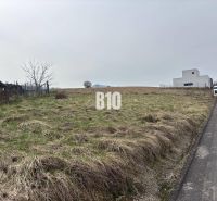 A plot for residential use in Rosina, next to the road, with a grassy surface and nearby buildings.