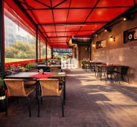 An outdoor terrace of a building in Čadca with tables, a red roof, and greenery.