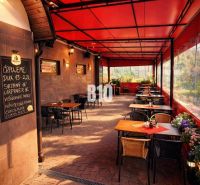 Covered terrace of a restaurant in the building of the town Čadca with brick paving, flowers, and tables.