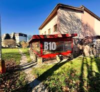 A building in Čadca with a garden, terrace, and red awning in sunny weather.