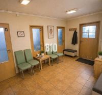 A waiting room with green chairs, magazines, and a clock. A floor with ceramic tiles.