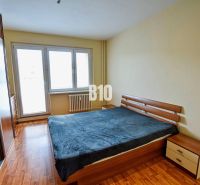 A bedroom in a 3-room apartment with a bed, wood-patterned flooring, and a built-in wardrobe.