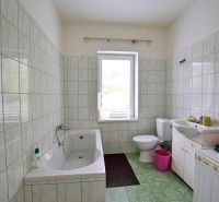 A bathroom in a family house with a bathtub, sink, and washing machine, tiled with light tiles.