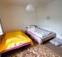 A room in a cottage with two beds, an open window, and a patterned carpet.
