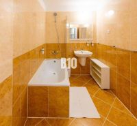 A bathroom in a studio apartment with light tiles, a bathtub, and a sink.