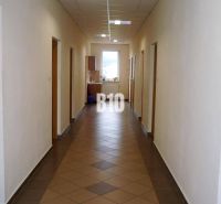 Hallway in an office with tiles, doors, and a window, interior lit by artificial light.