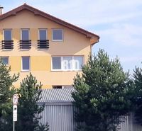 Yellow house with a sloped roof and windows behind trees near the office lines.