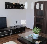 Living room with a television, shelves, a table, and a wooden decor floor in a 4-room apartment.