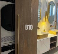 A bathroom with two sinks, a washing machine, and a dryer in a 3-room apartment, with a wooden decor floor.