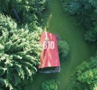 A cottage in Kunerad among the trees with a red roof and surrounding greenery.