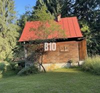 A wooden cottage in Kunerad with a red roof surrounded by forests and meadows.