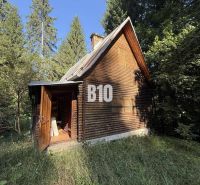 A wooden cabin in Kunerad surrounded by forest and blue sky.