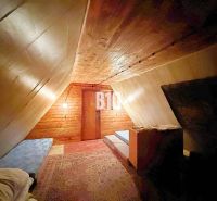 The attic of the cottage with a sloped ceiling, beds, and a wooden decor floor.