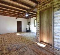 Interior of a cabin with wooden beams, flooring, and a stove for heating.