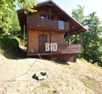 A wooden cabin in nature near Bytča, surrounded by trees and a fire pit.