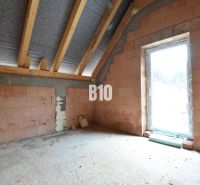 The ground floor of a family house showing raw brick walls and roof beams.