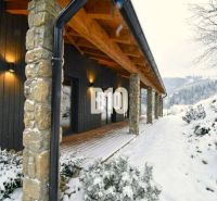 A cottage in the snowy landscape of Horná Mariková with stone pillars and wooden decor.