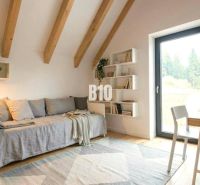 A bright room in a cabin with wooden beams, a couch, and a table on a floor with wooden decor.