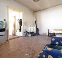 A room in a family house with a wooden decor floor, a stove, and furniture with floral fabric.
