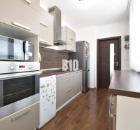 A kitchen in a 3-room apartment with a wooden decor floor and modern appliances.