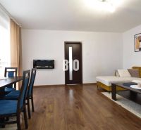 Living room in a three-room apartment with a wooden decor floor, sofa, and dining table.