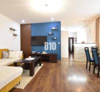 Living room with a sofa and a dining table in a 3-room apartment and a floor with a wooden decor.