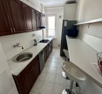 A narrow kitchen with a white countertop and wooden cabinets in a 3-room apartment.