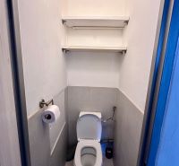 A bathroom in a 3-room apartment with two shelves on the wall.