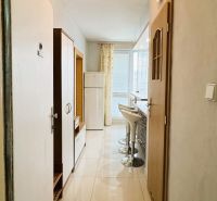 A narrow hallway in a one-room apartment with bar stools and a refrigerator.