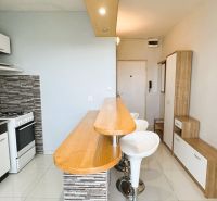 A kitchen with a bar counter and a tiled wall in a studio apartment.