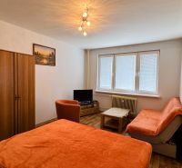 A room with furniture in a one-room apartment, a floor with a wooden decor, orange covers on the sofa.