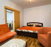 A room with a double bed, an orange armchair, and a wood-patterned floor.