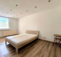 A bedroom with a light bed, chair, and wood-decorated floor in a studio apartment.