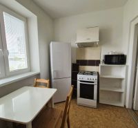 A kitchen of a 3-room apartment with a simple table, refrigerator, and stove.