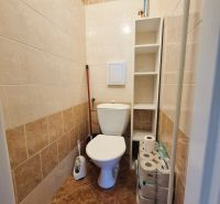 Bathroom with toilet, white tiles, and a shelf in a 3-room apartment.